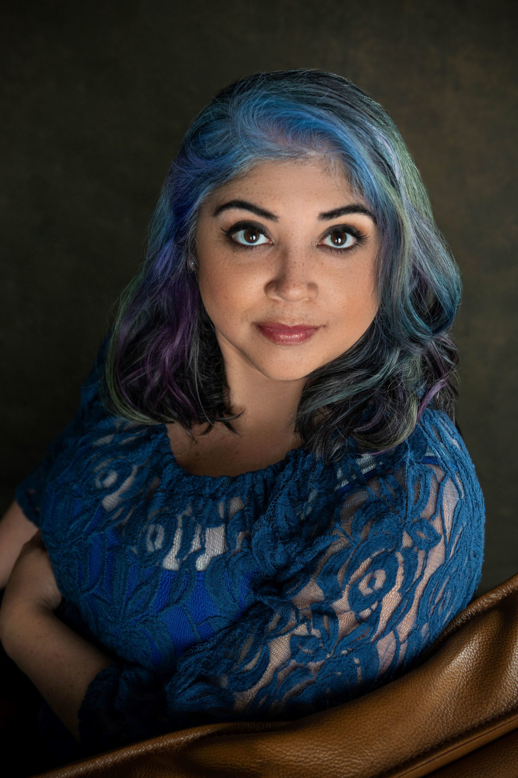 latina romance author in blue lace top sitting in a chair